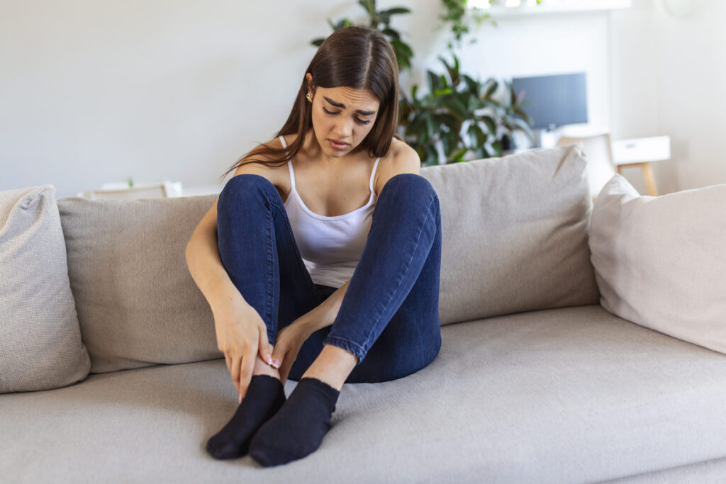 young woman in discomfort holding leg due to ankle pain